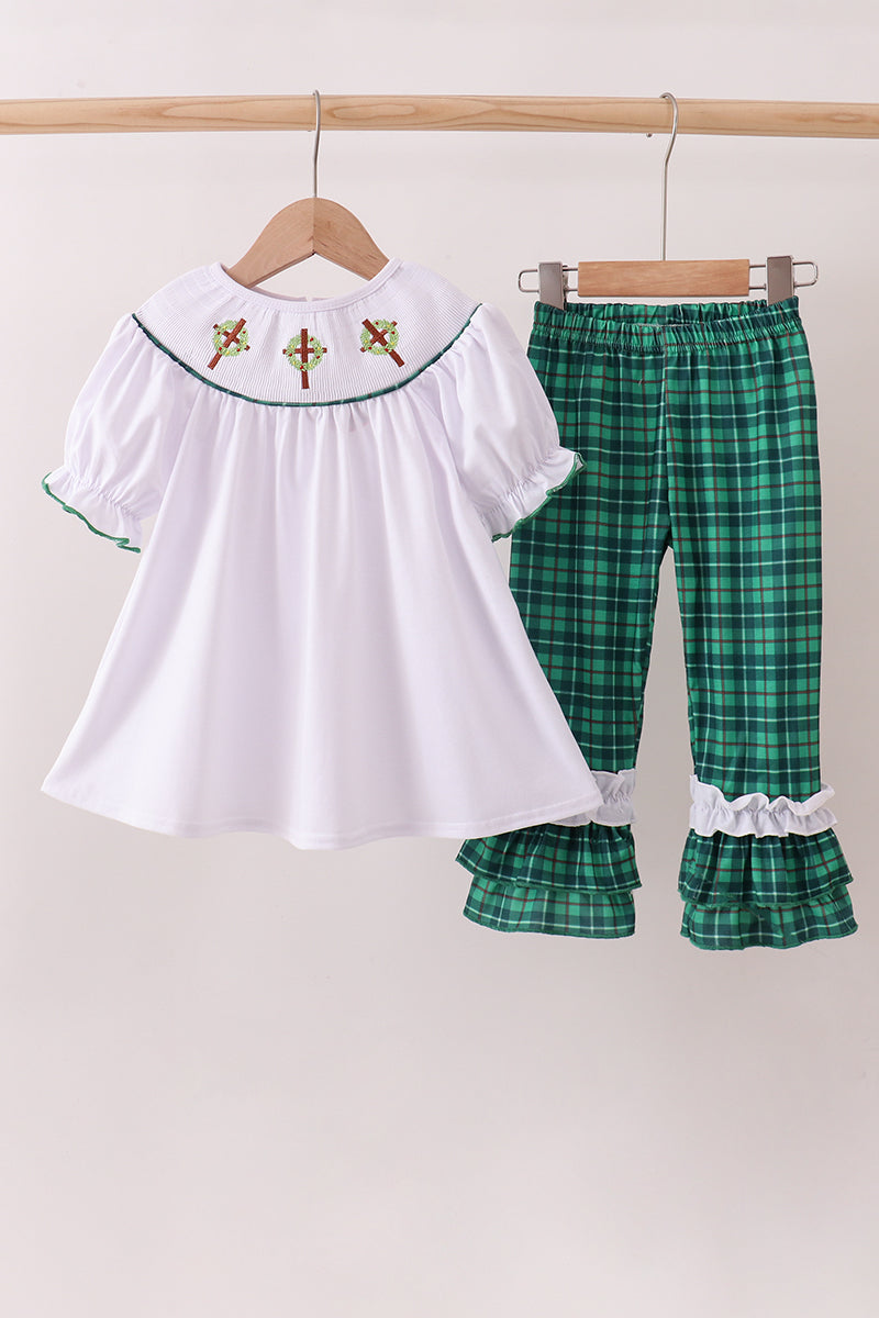White top with embroidered details and green plaid pants on hangers against a white background